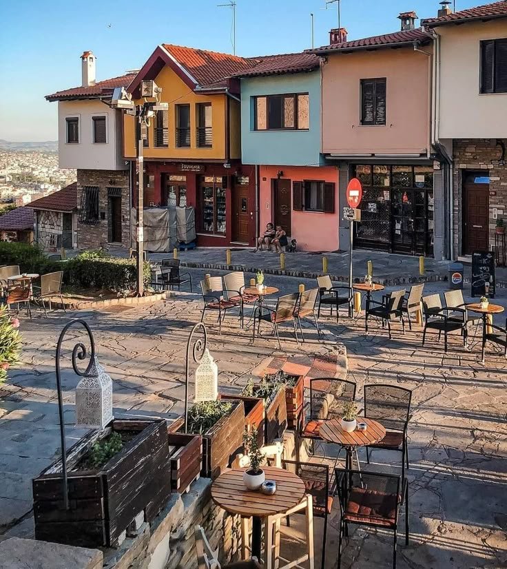 This may contain: several tables and chairs are outside in front of some buildings with many different colors on them