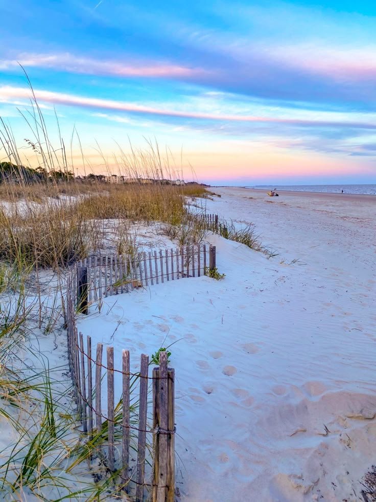This may contain: the beach is covered in white sand and sea oats as the sun goes down