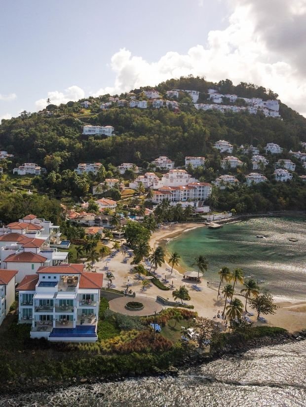 This may contain: an aerial view of houses on the beach and ocean in front of a hill side town