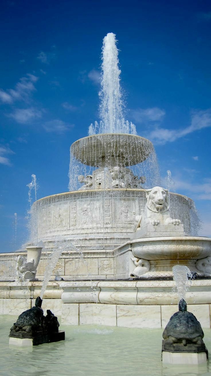This may contain: a fountain with water spouting from it's sides in front of a blue sky