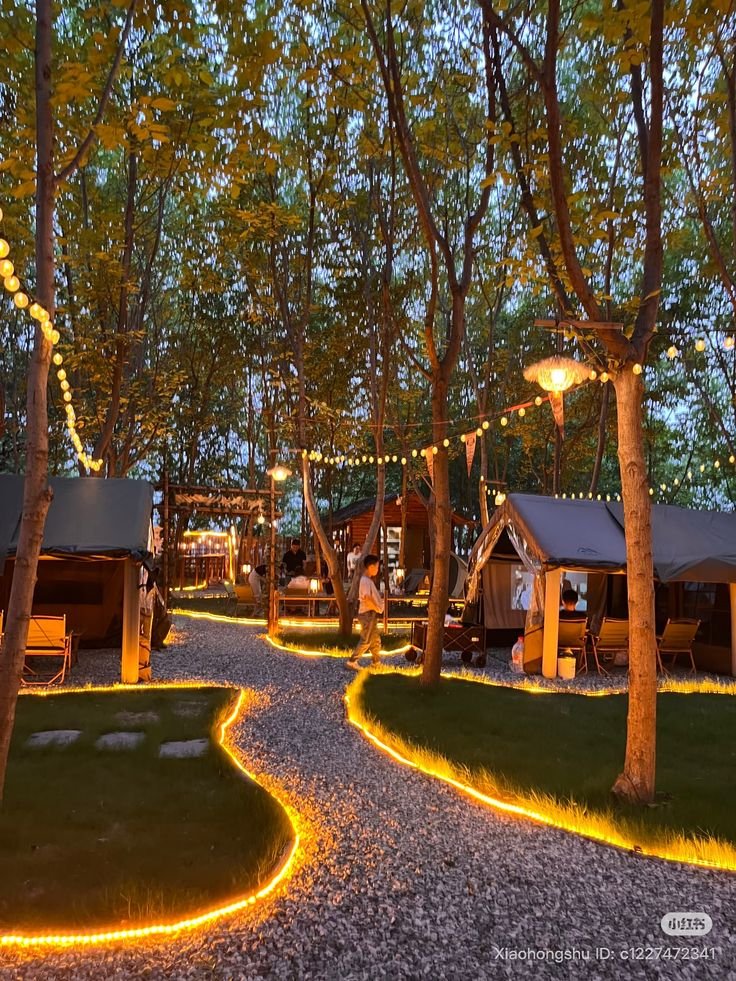 This may contain: an outdoor area with trees and lights in the night time, surrounded by small cabins
