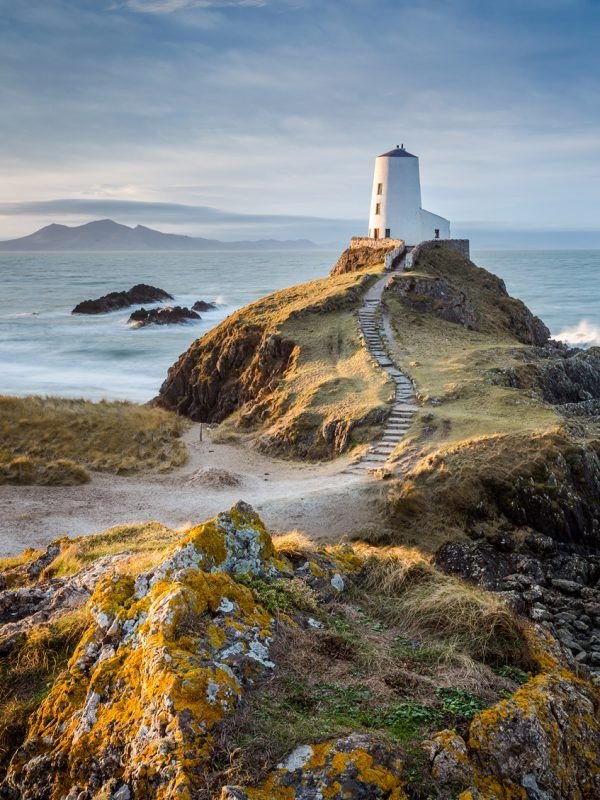 This may contain: a light house on top of a rocky hill next to the ocean with moss growing around it