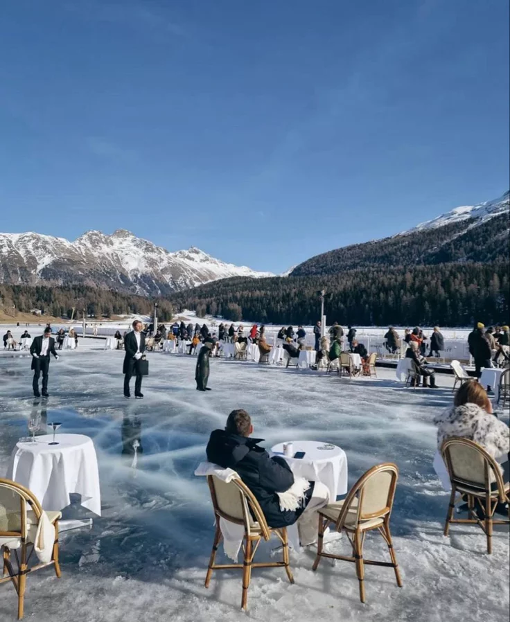 This may contain: people are sitting at tables on an ice covered lake with mountains in the back ground