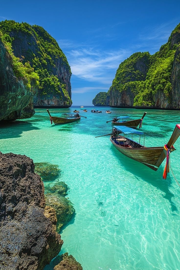 This may contain: three boats are anchored in the clear blue water near rocky cliffs and green trees on either side