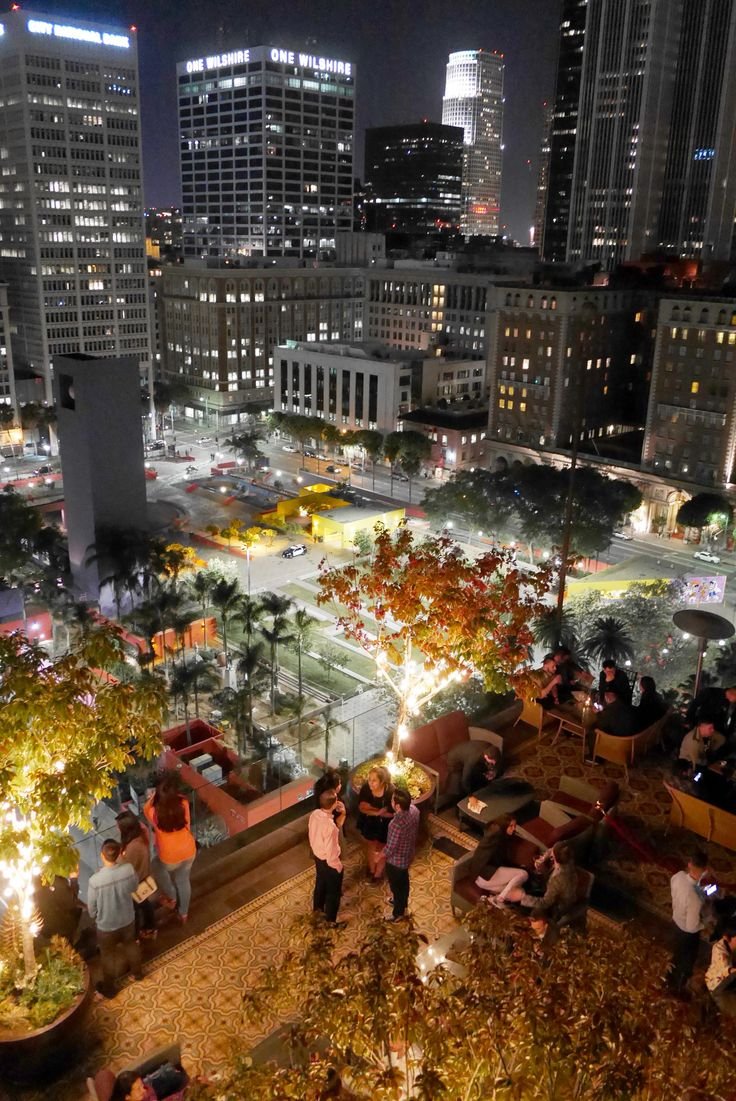 This may contain: people are sitting on benches in the city at night with their lights turned on and buildings lit up behind them