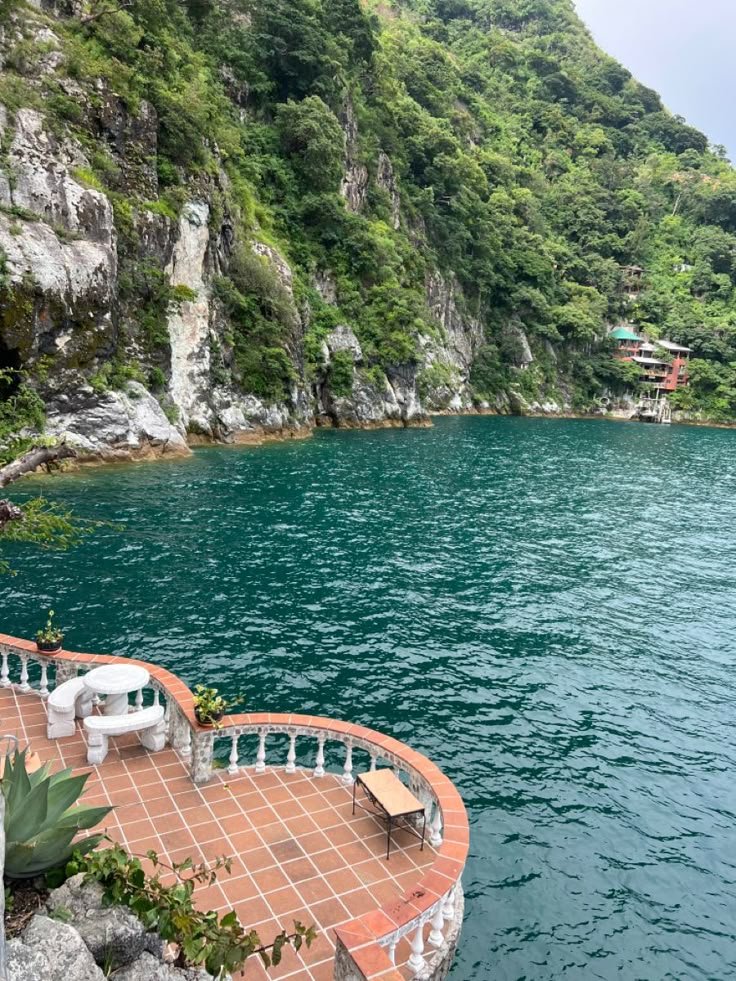 This may contain: the water is very clear and blue with some chairs on it in front of a cliff