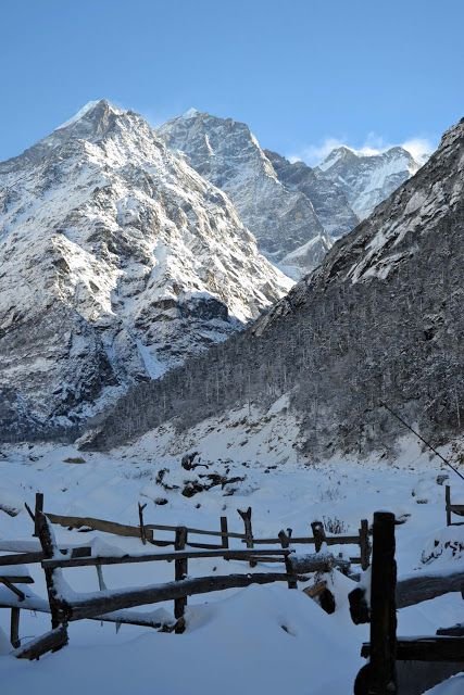 This may contain: the mountains are covered in snow and there is a wooden fence