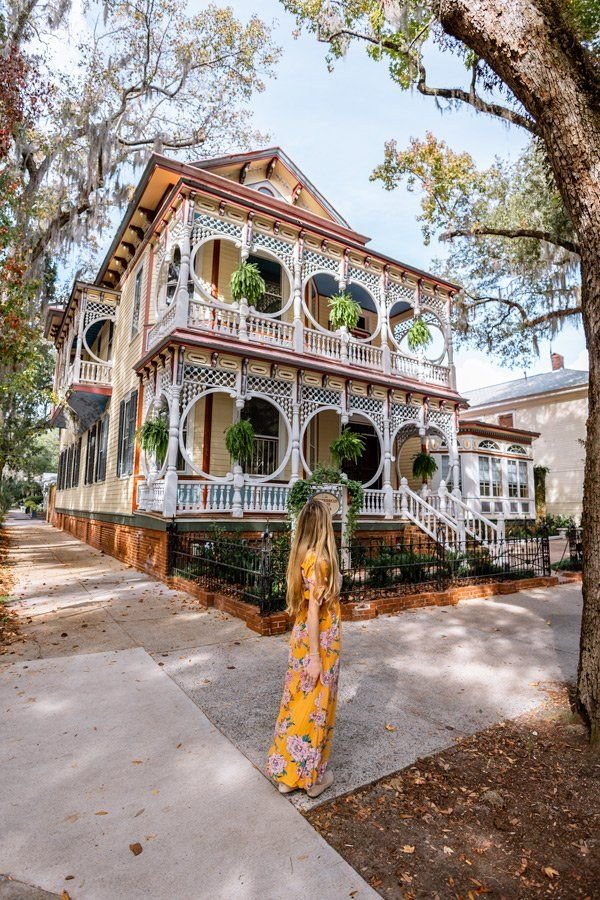 This may contain: a woman standing in front of a large house