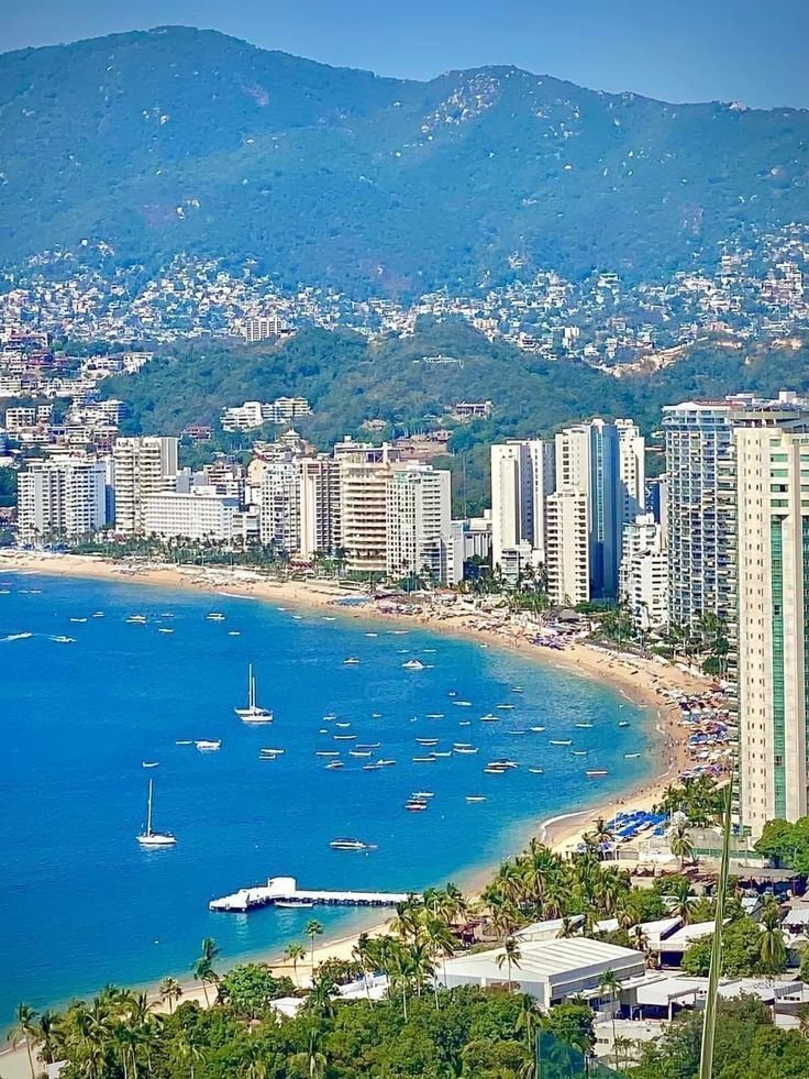 This may contain: an aerial view of a city and the ocean with sailboats in the water, surrounded by mountains