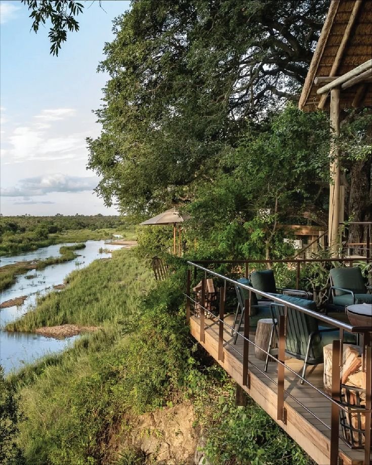 This may contain: an outdoor dining area overlooks the river and forest, while surrounded by greenery