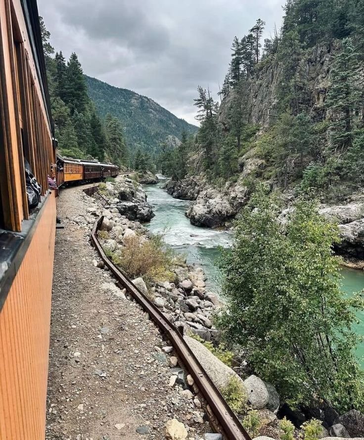 This may contain: a train traveling down tracks next to a river