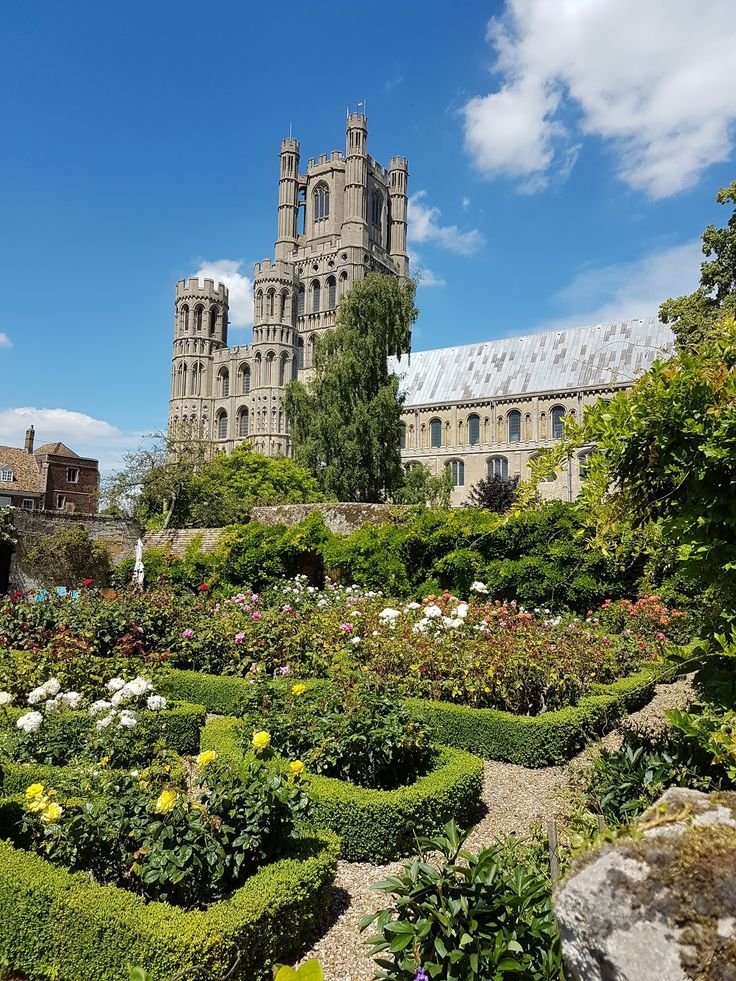 This may contain: a large building sitting on top of a lush green hillside next to flowers and trees