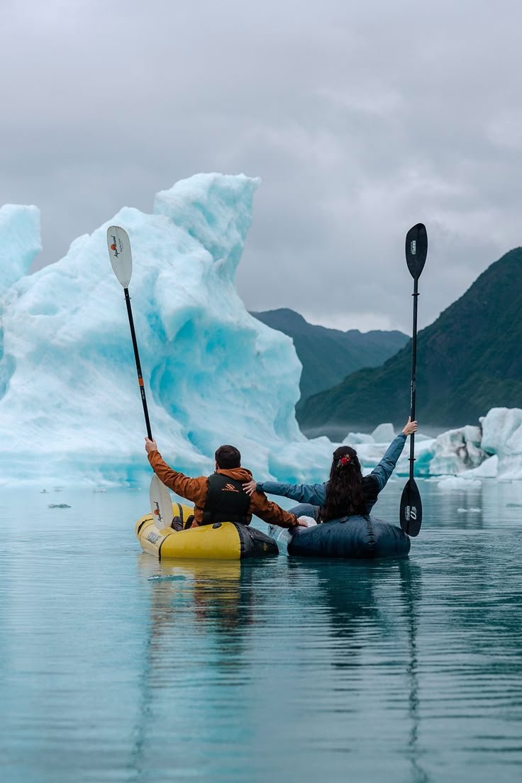 This may contain: two people in kayaks paddling past an iceberg