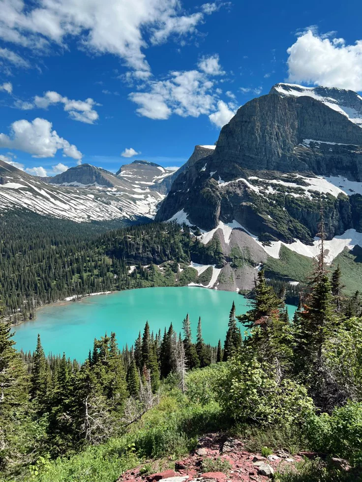 This may contain: a mountain lake surrounded by trees and snow covered mountains in the distance with blue water