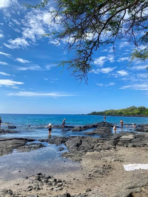 This may contain: people are standing on rocks near the ocean