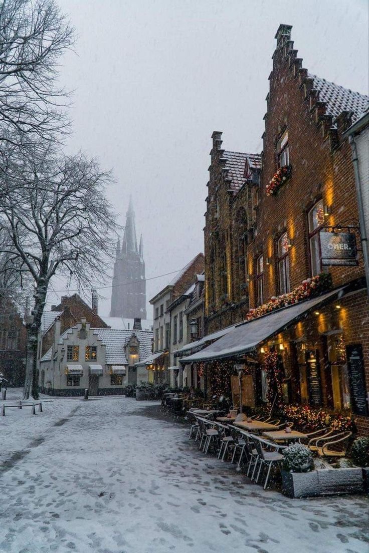 This may contain: a snowy street lined with buildings and tables