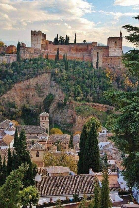 This may contain: an old castle on top of a hill with trees in the foreground and buildings below