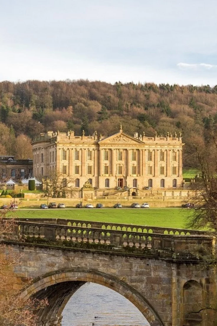 This may contain: an old stone bridge crossing over a river in front of a large building on a hill