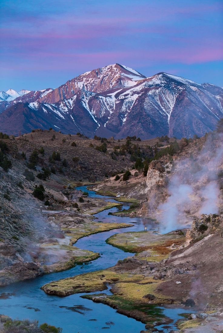This may contain: the mountains are covered in snow and steam as they rise from the ground to the water