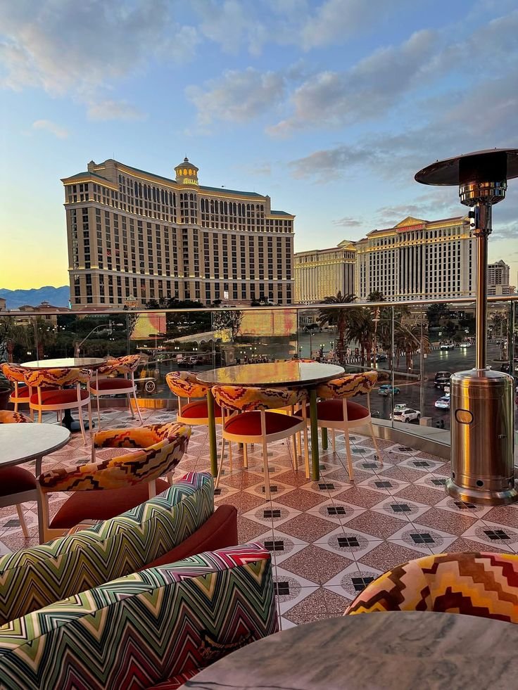 This may contain: an outdoor seating area with tables and chairs in front of the las vegas strip hotels