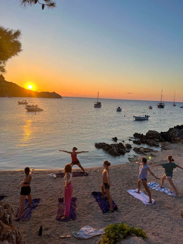 This may contain: a group of people doing yoga on the beach with boats in the water behind them