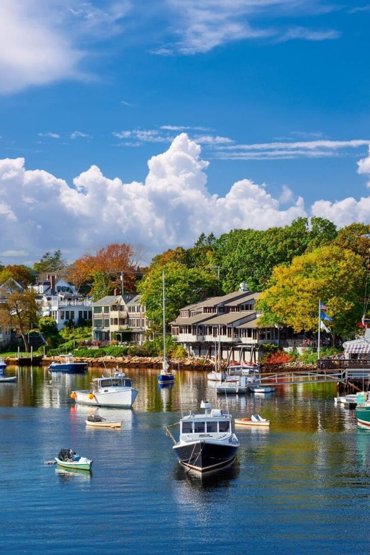 This may contain: several boats floating on the water in front of some houses and trees with clouds above them