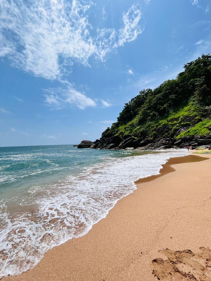 This may contain: a sandy beach next to the ocean under a blue sky with white clouds and green trees
