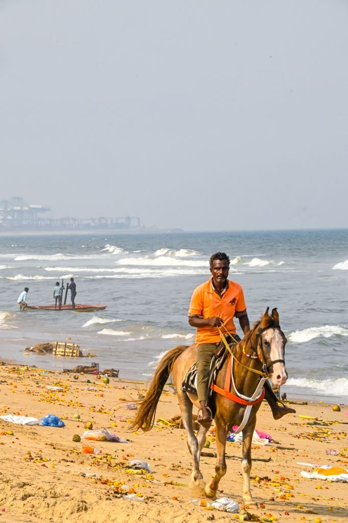 This may contain: a man riding on the back of a brown horse down a beach next to the ocean