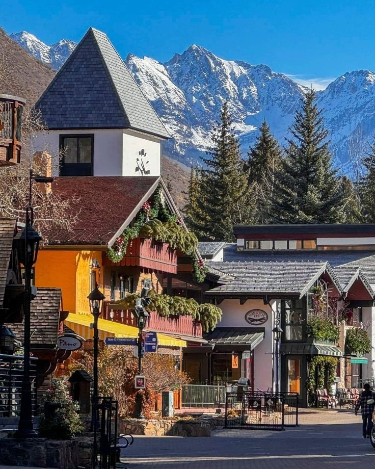 This may contain: a town with mountains in the background and people riding bikes on the street near it