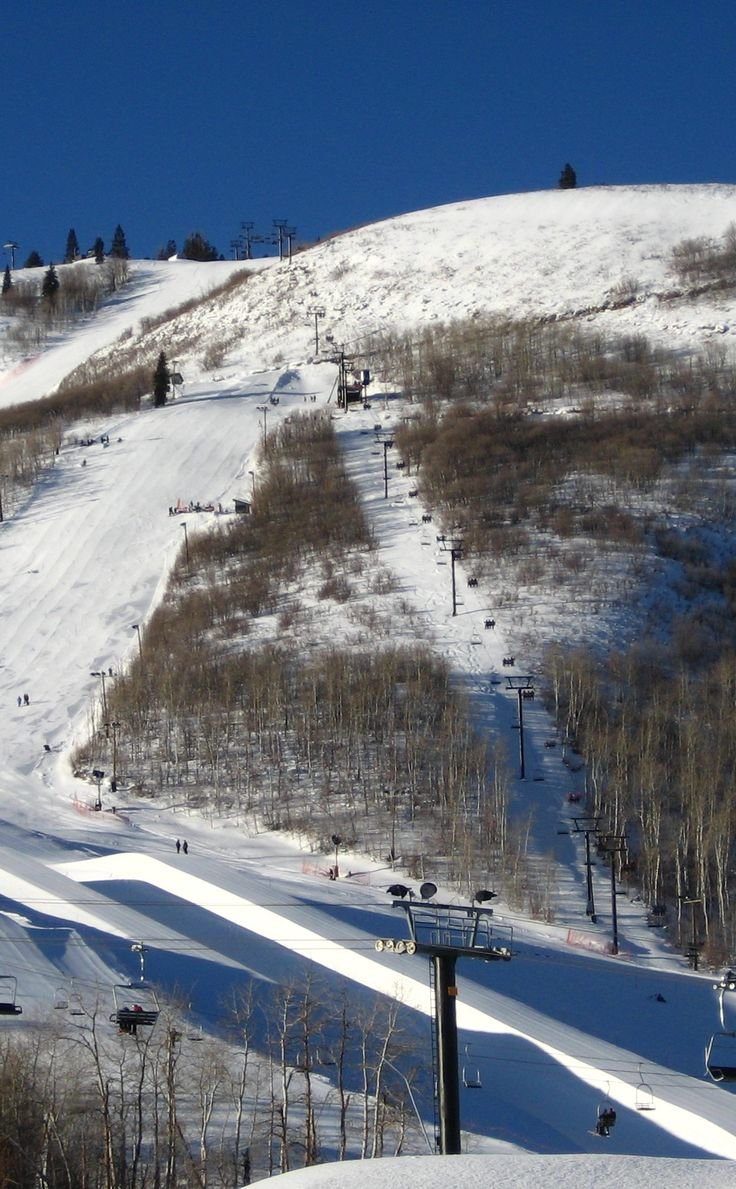 This may contain: a snow covered ski slope with people skiing down it