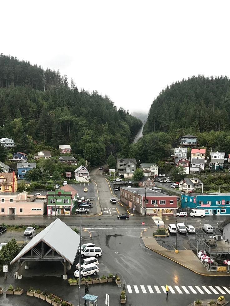 This may contain: an aerial view of a town with mountains in the back ground and cars parked on the street