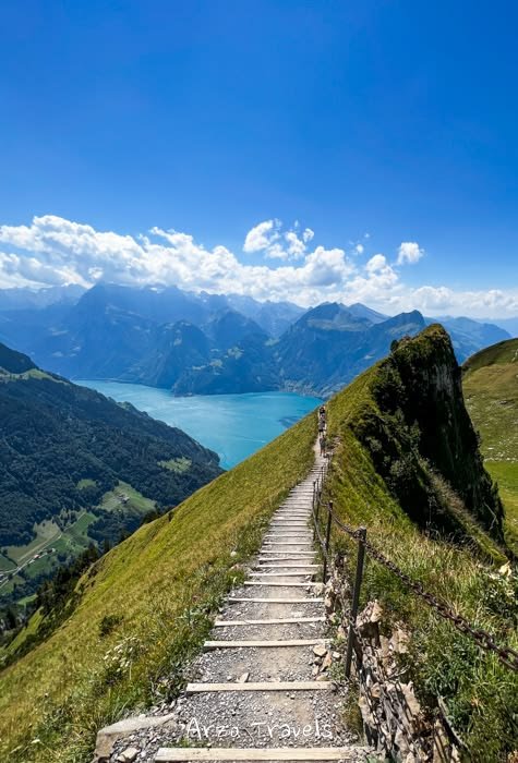 This may contain: stairs leading up to the top of a mountain with water in the distance and mountains on either side