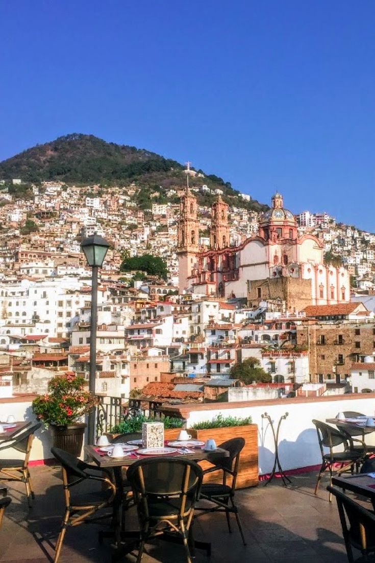 This may contain: an outdoor dining area with tables and chairs in front of a cityscape on a hill