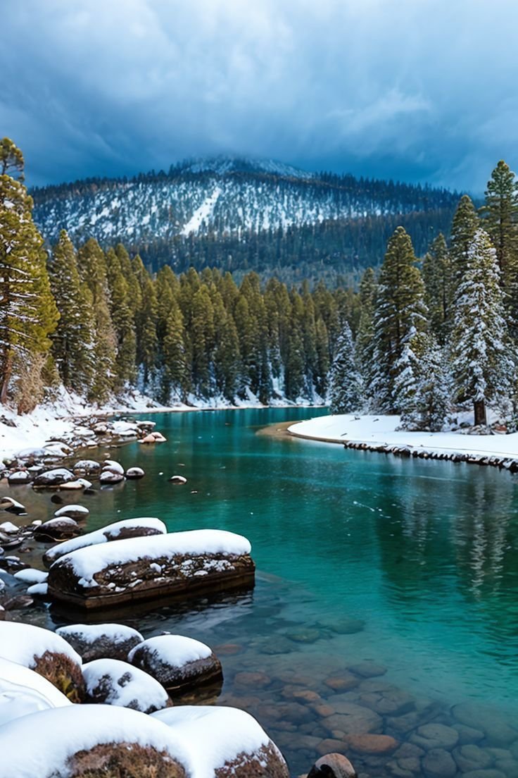 This may contain: a river surrounded by snow covered trees and rocks in the foreground with mountains in the background