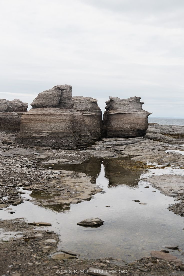 This may contain: some rocks are sitting on the shore by the water and one is in the middle of it