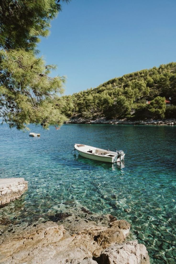 This may contain: a boat floating on top of a body of water next to a rocky shore covered in green trees
