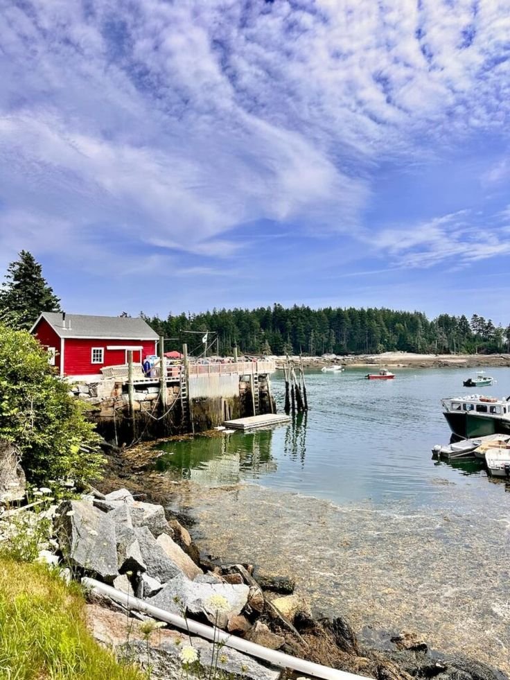 This may contain: boats are docked in the water next to a red house and some rocks on the shore