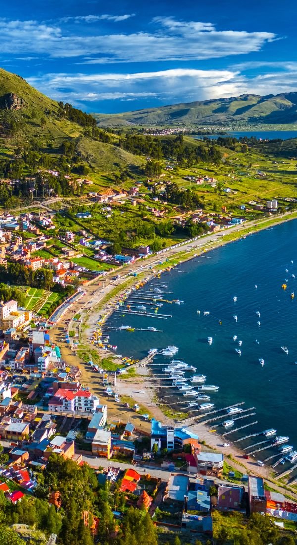 This may contain: an aerial view of a small town by the ocean with boats in the water and mountains behind it