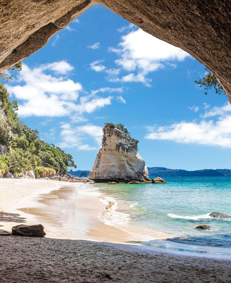 This may contain: the view from inside a cave looking out at the beach and ocean with rocks in the foreground