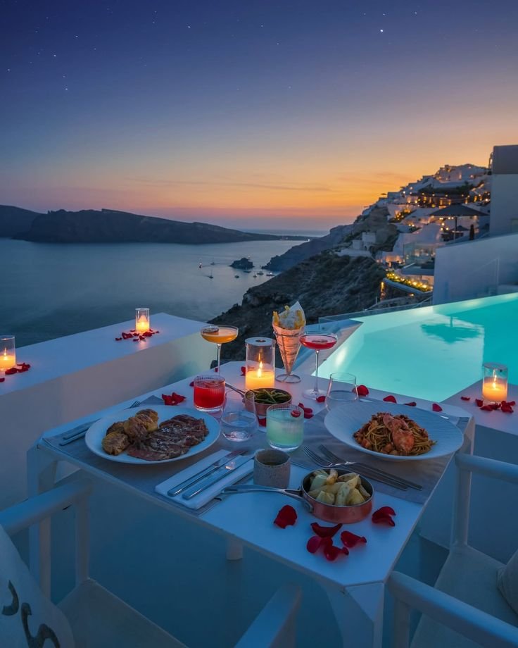 This may contain: an outdoor dining area with candles and plates of food on the table next to a swimming pool
