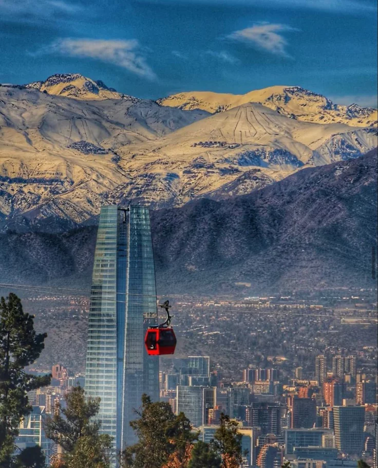 This may contain: a red cable car going up the side of a mountain with snow capped mountains in the background