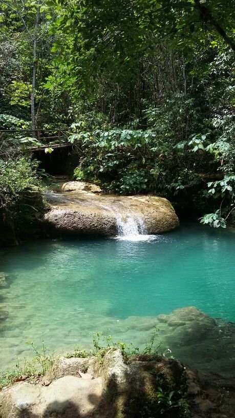 This may contain: there is a small waterfall in the middle of this pool with blue water and rocks