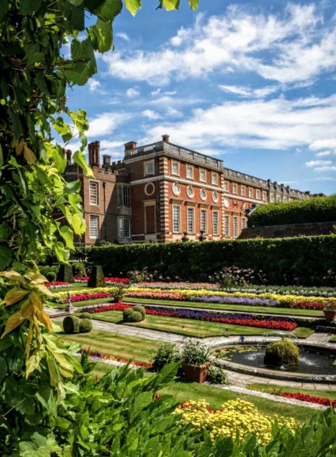 This may contain: a large building with many flowers in the foreground and trees on either side of it