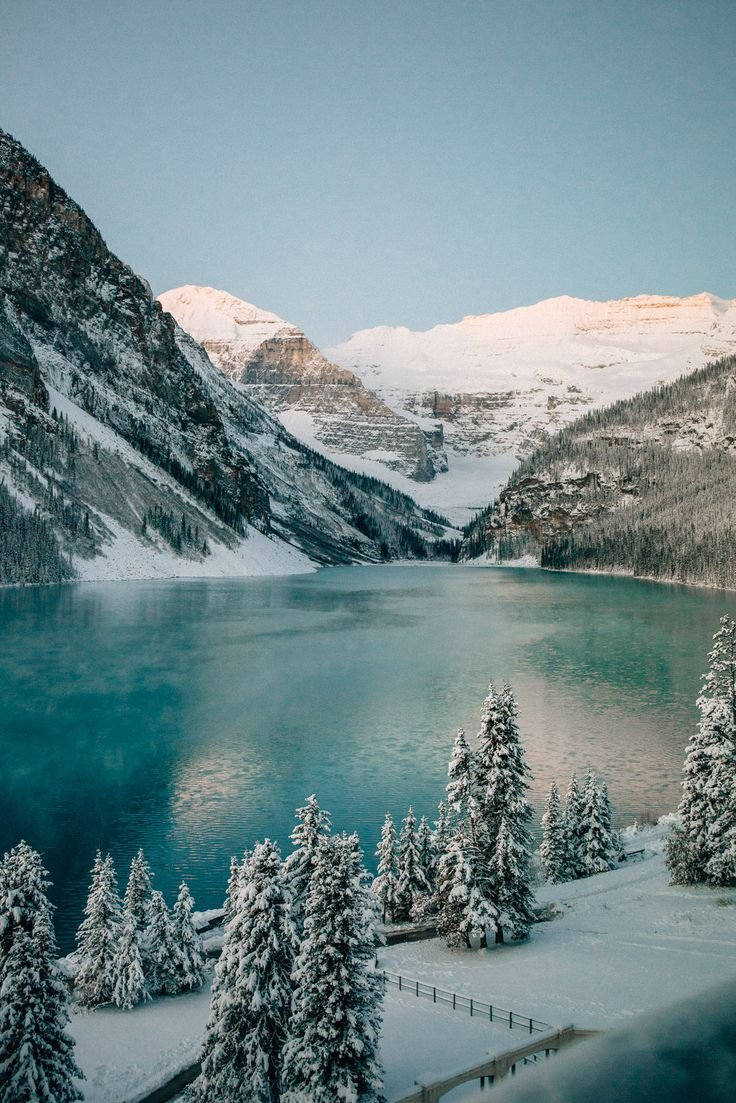 This may contain: a lake surrounded by snow covered trees and mountains