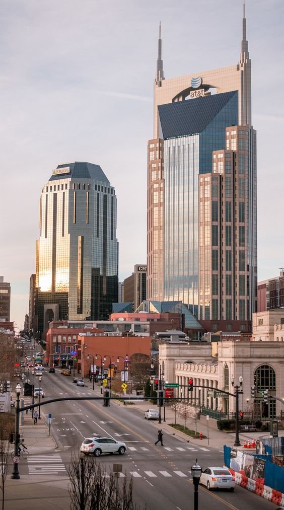 This may contain: a city street with tall buildings on both sides and cars driving down the road in front