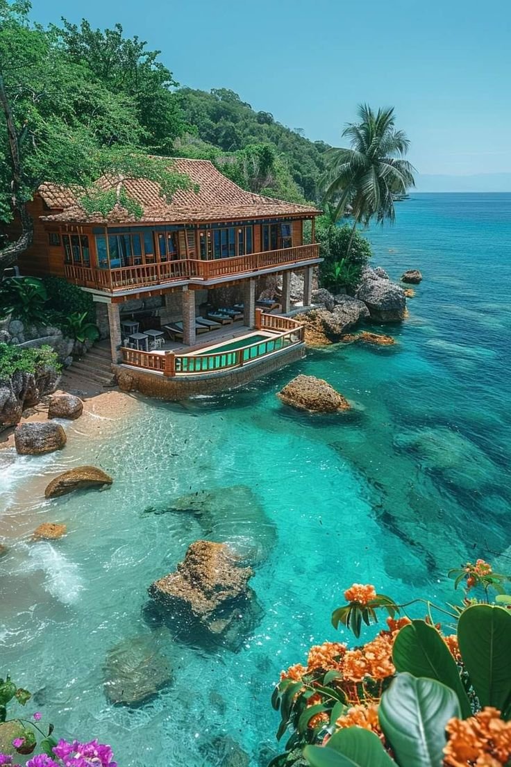 This may contain: a house sitting on top of a lush green hillside next to the ocean with blue water