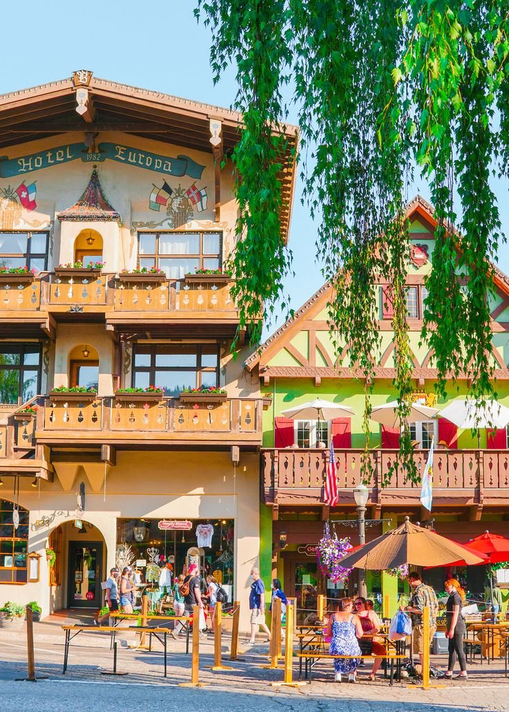 This may contain: people are sitting at tables in front of a multi - colored building with balconies and umbrellas