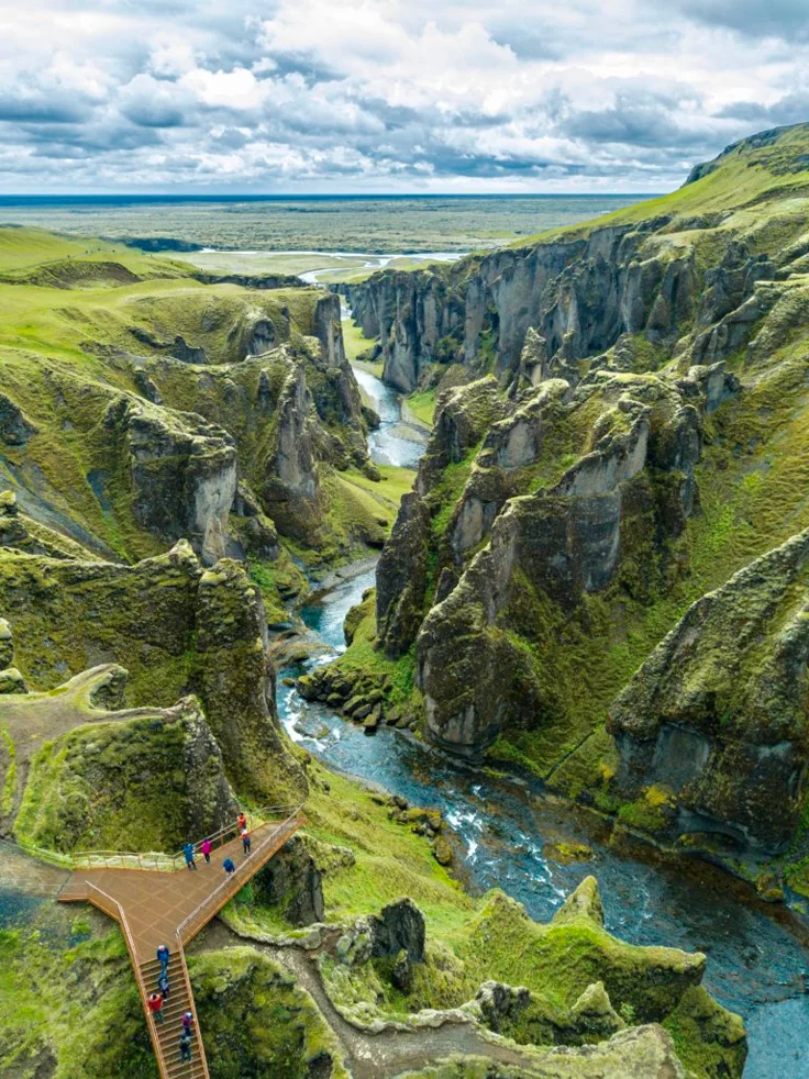 This may contain: people are standing on a bridge over a river in the middle of a valley surrounded by mountains
