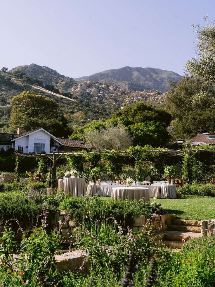 This may contain: an outdoor table set up in the middle of a garden with mountains in the background
