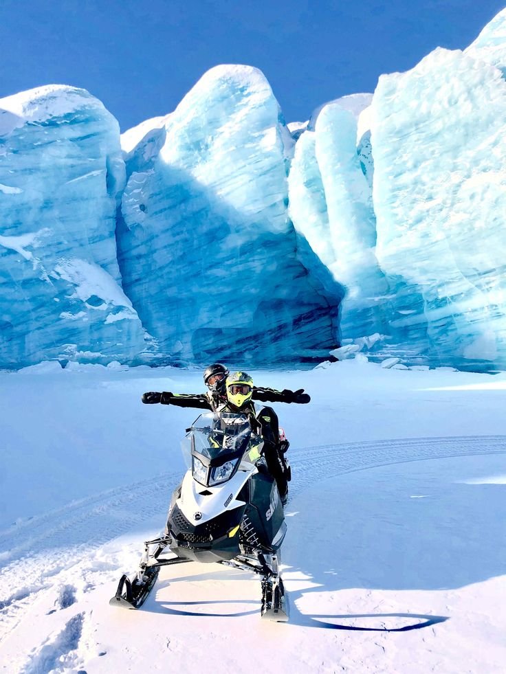 This may contain: two people riding on the back of a snowmobile in front of icebergs